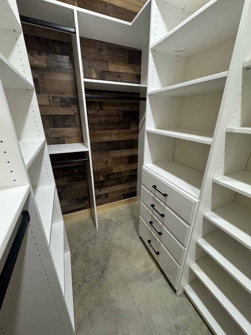 Custom walk-in closet with white shelving, drawers, and a wood accent wall