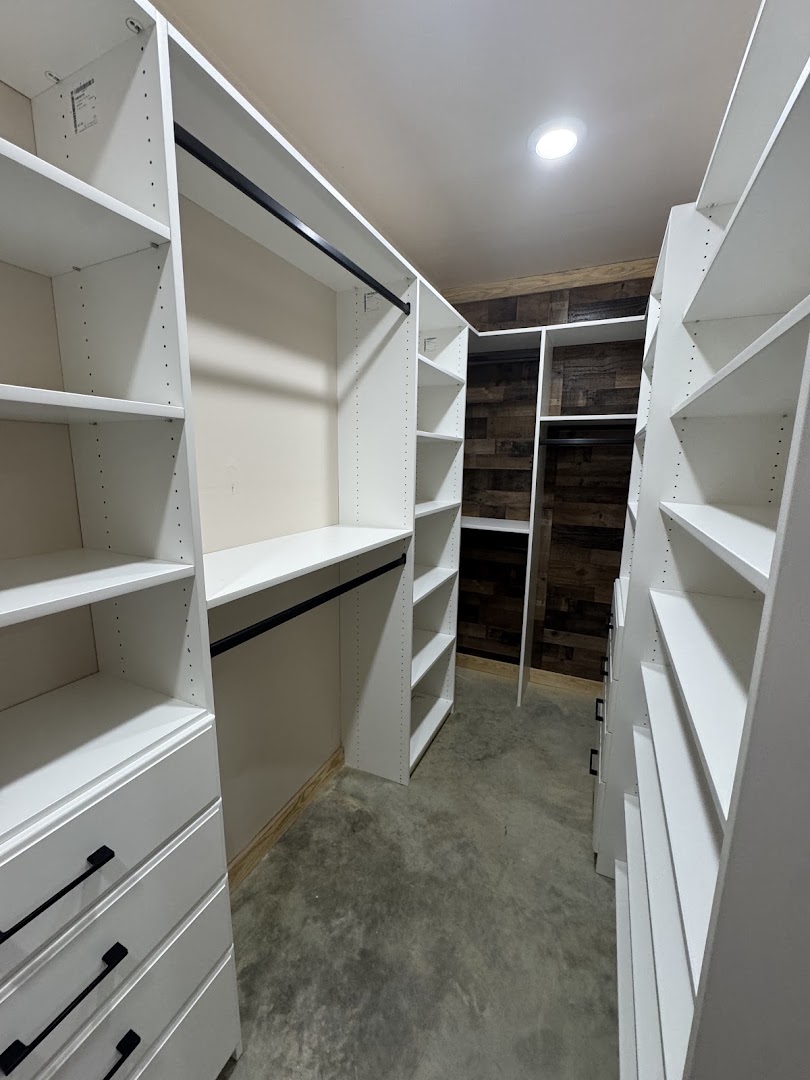 White walk-in closet shelving with hanging rods, drawers, and a wood accent wall