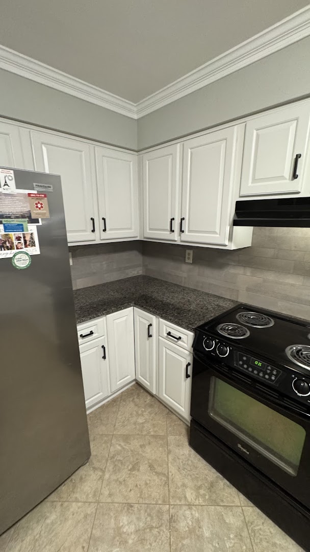 Corner view of white kitchen cabinets with black hardware and a tiled backsplash